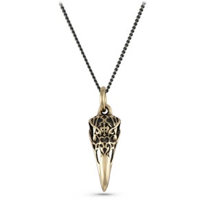 May include: A gold-toned pendant necklace with a detailed, filigree raven skull design. The pendant is attached to a black chain.
