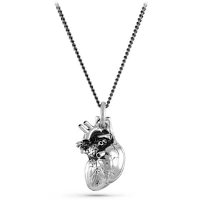 May include: A silver anatomical heart pendant necklace on a black chain. The heart is detailed and realistic.