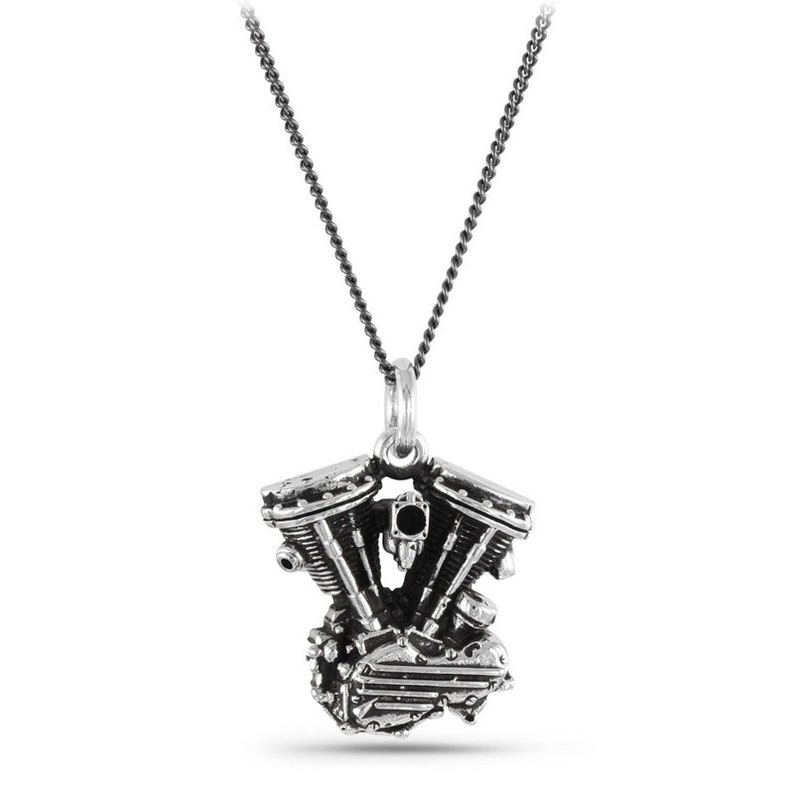 May include: A silver necklace featuring a detailed pendant shaped like a motorcycle engine. The pendant has a black stone in the centre.