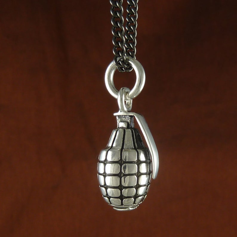 May include: A silver grenade pendant necklace with a black chain. The pendant is detailed with a textured surface and a small ring at the top.