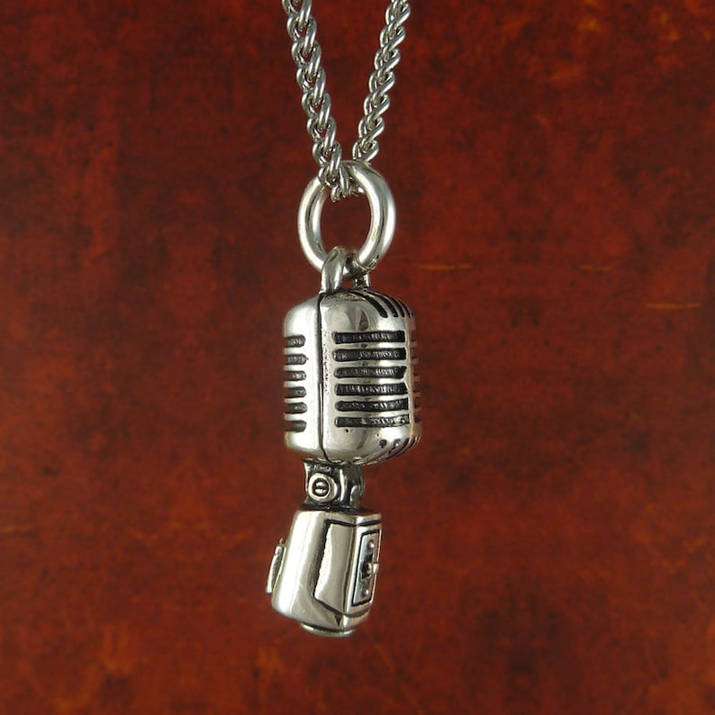May include: Silver necklace with a vintage microphone pendant. The microphone is detailed with a silver finish and has a textured design.