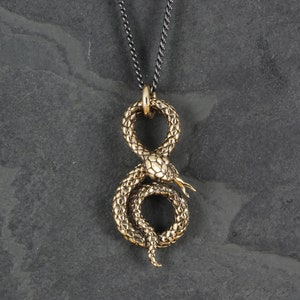 Op de afbeelding: Een gouden slangenhangerketting met een zwarte ketting. De slang is in de vorm van een acht gewikkeld.