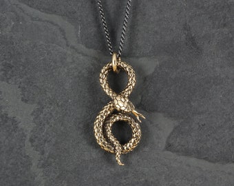 May include: A gold-toned snake pendant necklace with a black chain. The snake is coiled in a figure eight shape.