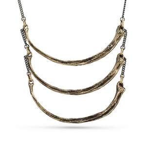 May include: A gold necklace with three curved, textured pieces that resemble bone. The necklace is attached to a black chain.