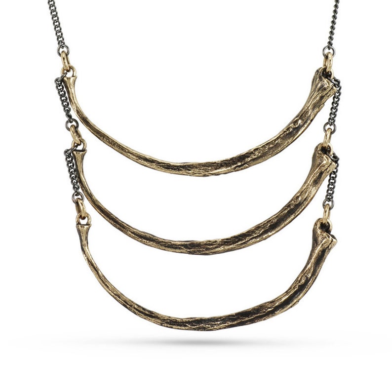 May include: A gold necklace featuring three curved, textured pieces reminiscent of bone. The necklace is attached to a black chain.