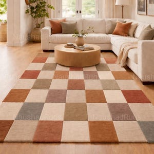 May include: A large, rectangular area rug with a checkerboard pattern in shades of beige, brown, and rust. The rug is placed in a living room with a white sectional sofa and a wooden coffee table. The rug adds warmth and texture to the space.