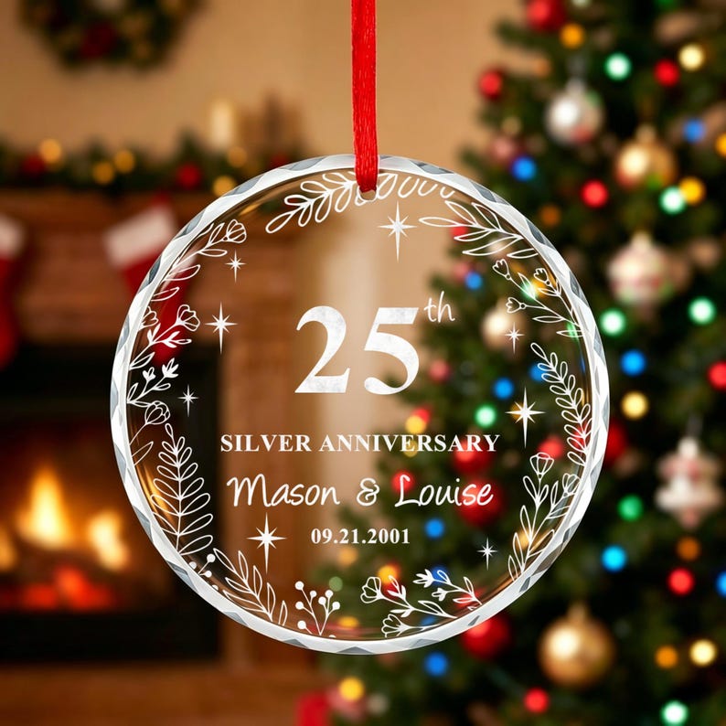 K&ouml;nnte beinhalten: Ein kreisf&ouml;rmiges Ornament aus klarem Acryl, das an einem roten Band h&auml;ngt. Das Design zeigt wei&szlig;e, gravierte Blumenranken, Sterne und den Text 25th SILVER ANNIVERSARY, Mason & Louise sowie 09.21.2001. Der Rand ist facettiert geschliffen.