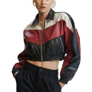 Peut inclure: Veste courte en cuir avec un design color block. La veste présente une palette de couleurs noire, rouge et blanche avec une fermeture éclair sur le devant et un col. Les manches sont longues et se terminent par des poignets élastiques.