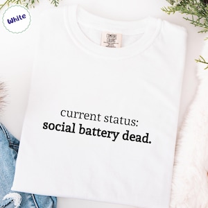 May include: White crew neck t-shirt with the text "current status: social battery dead" in black. The shirt has a Comfort Colors tag and is displayed on a white surface.
