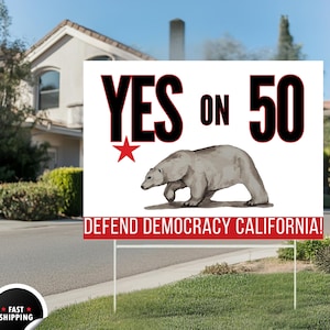 May include: A white yard sign with the text "YES ON 50" in black, a red star, and a drawing of a bear. The sign also reads "DEFEND DEMOCRACY CALIFORNIA!" in red. The sign is on a lawn.