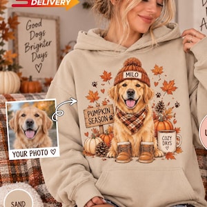 May include: A sand-colored hooded sweatshirt featuring a graphic of a golden retriever wearing a beanie with the name MILO, a plaid scarf, and boots. The design includes autumn leaves, pumpkins, a sign reading PUMPKIN SEASON, and a mug labeled COZY DAYS.