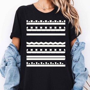 May include: Black t-shirt with a white geometric pattern. The design features horizontal lines, squares, and zigzags. The shirt has short sleeves and a crew neck. A denim jacket is draped over the shoulders.