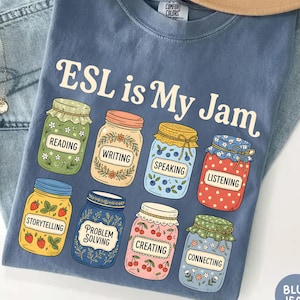 May include: A blue t-shirt featuring the text "ESL is My Jam" above eight illustrated jars. Each jar contains a different pattern and a label with the words reading, writing, speaking, listening, storytelling, problem solving, creating, and connecting.
