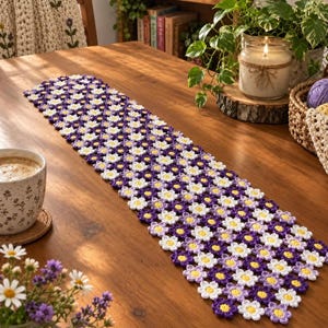 Può includere: Un runner da tavola rettangolare realizzato con fiori all'uncinetto interconnessi in tonalità viola, lavanda e bianco con centri gialli. Il motivo floreale è disposto in una griglia ripetitiva, creando una superficie strutturata per tutta la lunghezza.
