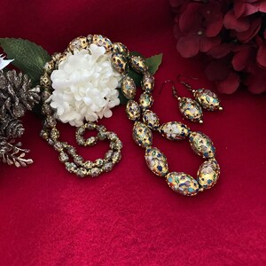 Puede incluir: Un collar y pendientes de oro con cuentas ovaladas decoradas con motivos florales de esmalte de colores. Las cuentas est&aacute;n sobre un fondo de terciopelo rojo.
