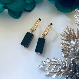 May include: A pair of gold earrings with black rectangular stones and clear crystal accents.