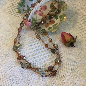 May include: A double strand necklace with iridescent brown and clear glass beads. The necklace is displayed in a white ceramic dish with a floral design.