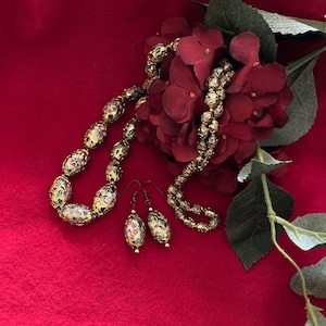 Puede incluir: Un collar y pendientes a juego de oro con dise&ntilde;os florales de esmalte de colores. El collar y los pendientes est&aacute;n sobre un fondo rojo con una flor roja.