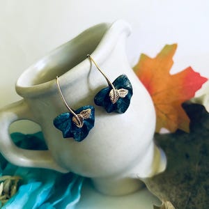 May include: A pair of dangle earrings with a teal blue leaf design and gold leaf accents.