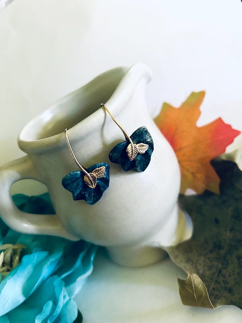 May include: A pair of dangle earrings with a teal blue leaf design and gold leaf accents.