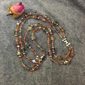 May include: A multi-strand necklace with brown, orange, and clear iridescent beads. The necklace is made of small seed beads and larger faceted beads.