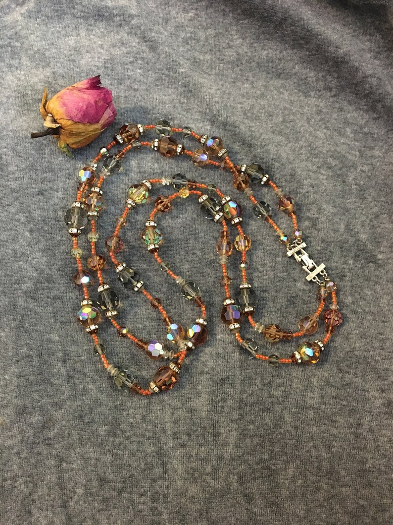 May include: A multi-strand necklace with brown, orange, and clear iridescent beads. The necklace is made of small seed beads and larger faceted beads.