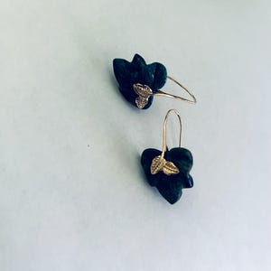 May include: A pair of gold earrings with dark green flower-shaped pendants and gold leaf accents.