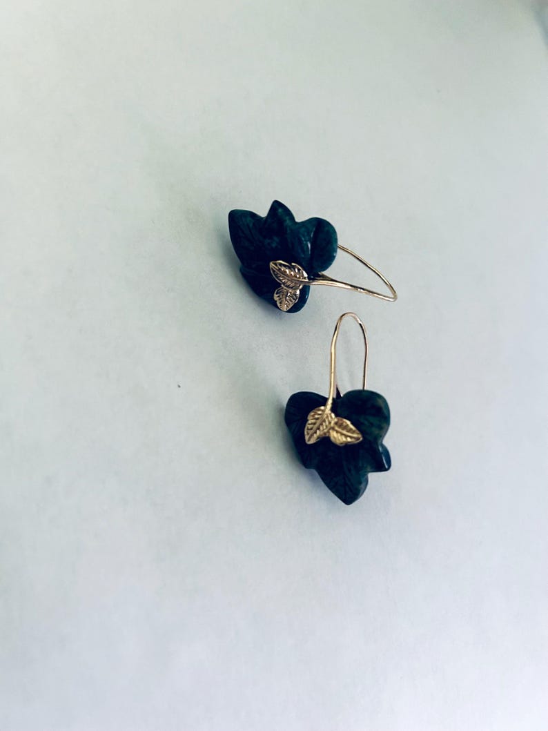 May include: A pair of gold earrings with dark green flower-shaped pendants and gold leaf accents.