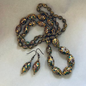 Puede incluir: Un collar y pendientes de oro con cuentas de forma ovalada. Las cuentas est&aacute;n decoradas con motivos florales en tonos rosa, azul, verde y blanco.