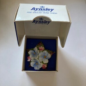 May include: A blue and white porcelain flower brooch in a star shape, in a white box with the words "Aysnley Established 1775 Fine English Bone China" on the lid.