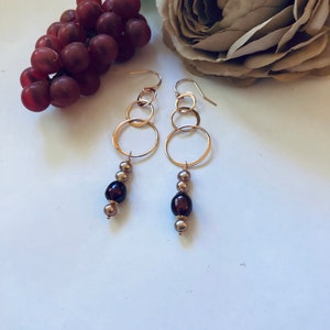 May include: Gold hoop earrings with a dangling chain of brown and gold beads.