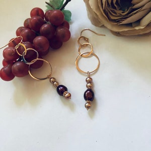 May include: Gold hoop earrings with three interconnected circles and a dangling chain of brown and gold beads.