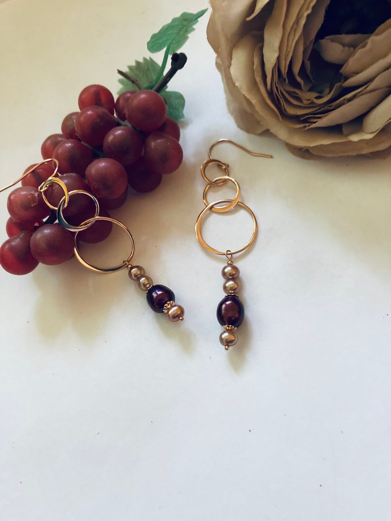 May include: Gold hoop earrings with three interconnected circles and a dangling chain of brown and gold beads.