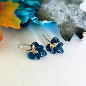 May include: A pair of green leaf-shaped earrings with gold accents. The earrings are made of a dark green stone with a marbled pattern.