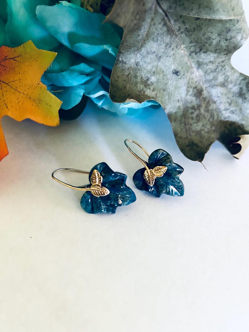 May include: A pair of green leaf-shaped earrings with gold accents. The earrings are made of a dark green stone with a marbled pattern.