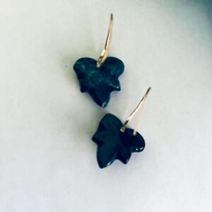 May include: A pair of gold earrings with dark green leaf-shaped pendants.