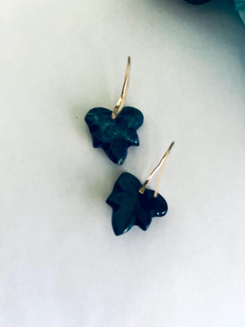 May include: A pair of gold earrings with dark green leaf-shaped pendants.