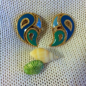 May include: A pair of gold tone earrings with blue and green enamel. The earrings are shaped like a teardrop and have a geometric design.