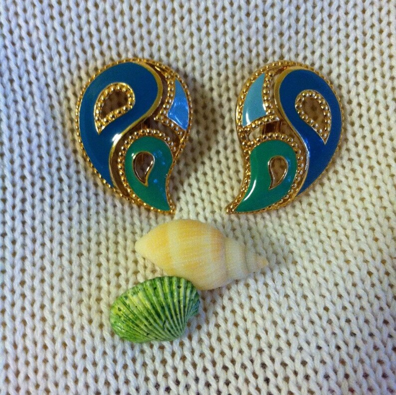 May include: A pair of gold tone earrings with blue and green enamel. The earrings are shaped like a teardrop and have a geometric design.