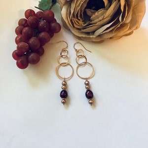 May include: Gold hoop earrings with three hoops on each earring and a dangling strand of three brown pearls.
