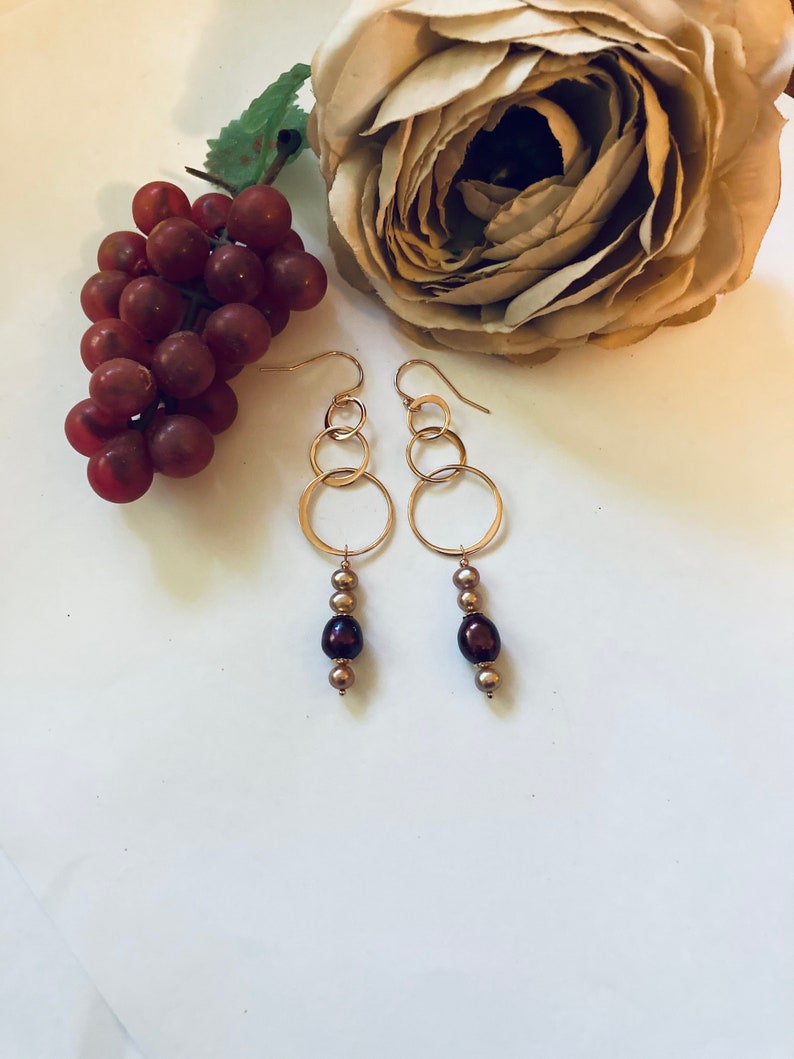 May include: Gold hoop earrings with three hoops on each earring and a dangling strand of three brown pearls.