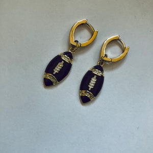 May include: A pair of gold hoop earrings with black enamel football charms. The football charms have white diamond accents.