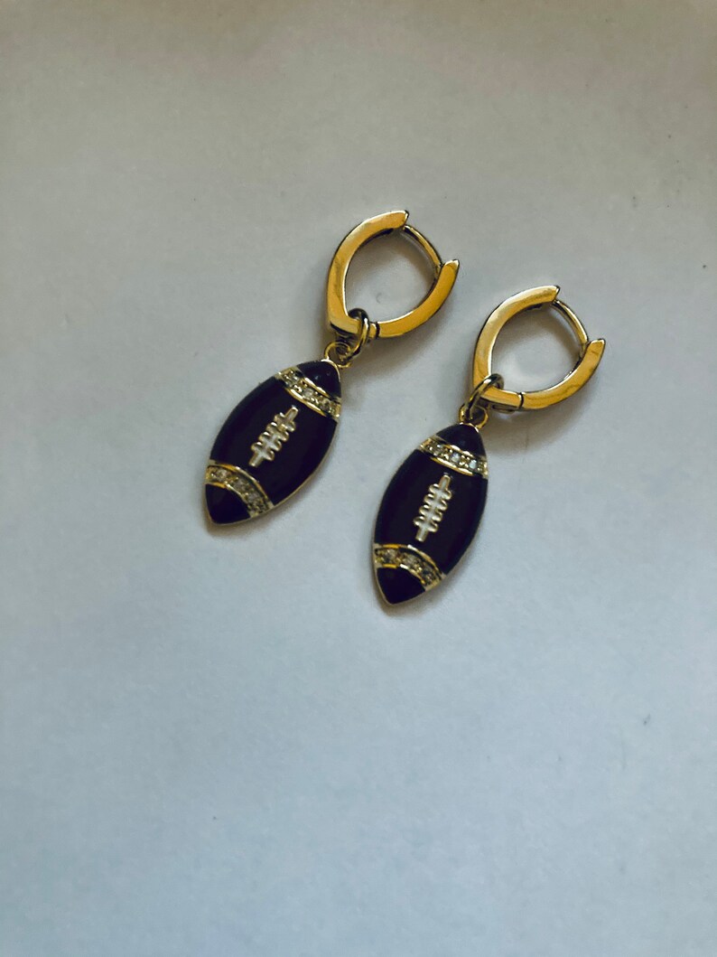 May include: A pair of gold hoop earrings with black enamel football charms. The football charms have white diamond accents.