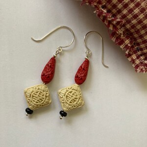 Puede incluir: Un par de pendientes con cuentas talladas en rojo y blanco y detalles negros. Los pendientes est&aacute;n hechos de plata y tienen un dise&ntilde;o de gota.