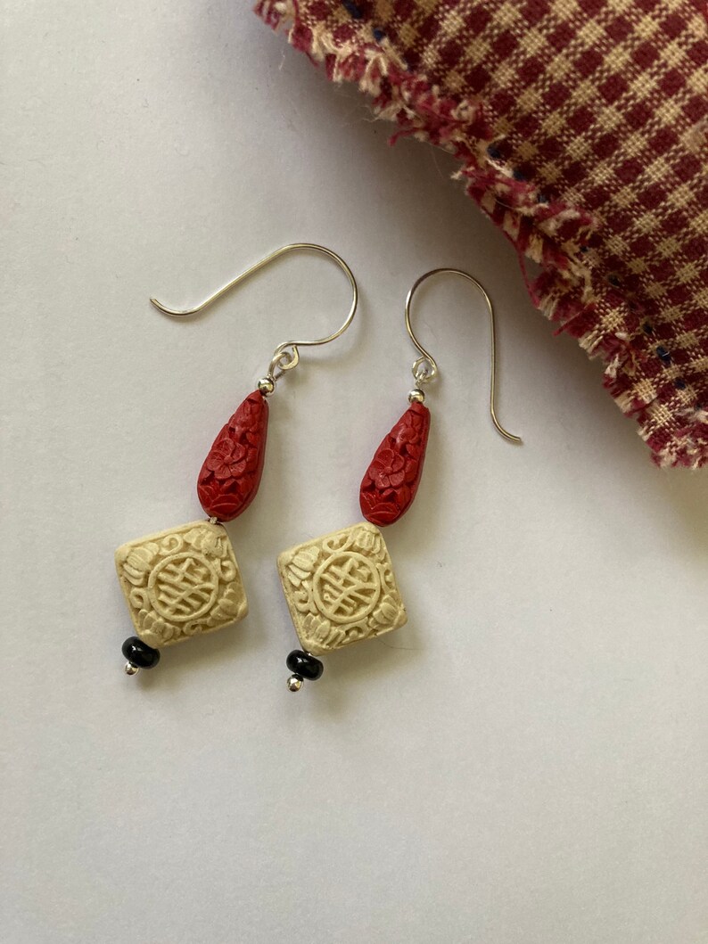 Puede incluir: Un par de pendientes con cuentas talladas en rojo y blanco y detalles negros. Los pendientes est&aacute;n hechos de plata y tienen un dise&ntilde;o de gota.