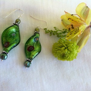 May include: A pair of green glass earrings with silver hooks and pearl accents. The earrings are shaped like a teardrop and have a swirl pattern.