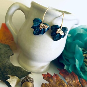 May include: A pair of dangle earrings with a blue leaf design and gold accents. The leaves are textured and have a natural look.
