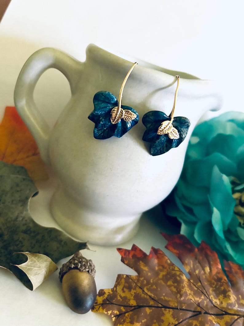 May include: A pair of dangle earrings with a blue leaf design and gold accents. The leaves are textured and have a natural look.