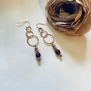 May include: Gold hoop earrings with a dangling chain of brown and gold beads.
