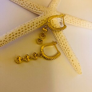 May include: A pair of gold hoop earrings with dangling heart charms. Each heart charm is adorned with small, clear cubic zirconia stones.